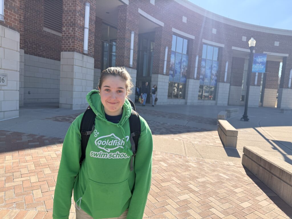 My daughter wearing a green sweatshirt with sunshine and a college building behind her